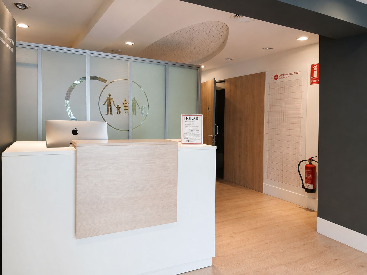 Recepción de Chiropractic First Barcelona con mostrador blanco y detalles de madera